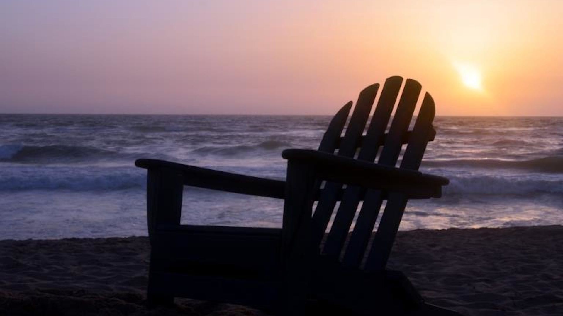 A Person Sitting On A Bench Overlooking The Ocean At Sunset